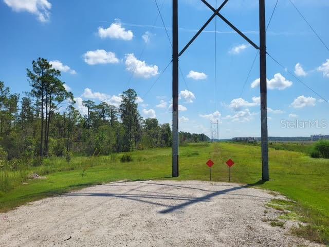 A gravel path leads toward a utility pole and power lines in a grassy field — S APOPKA VINELAND, ORLANDO, FL