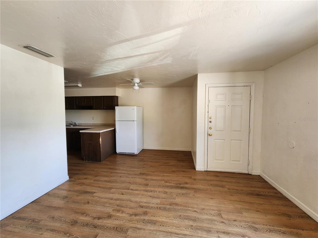 An open-concept room features wood-look flooring, a white refrigerator, and a small kitchen area — 719 SW 70TH TERRACE UNIT 5, GAINESVILLE, FL