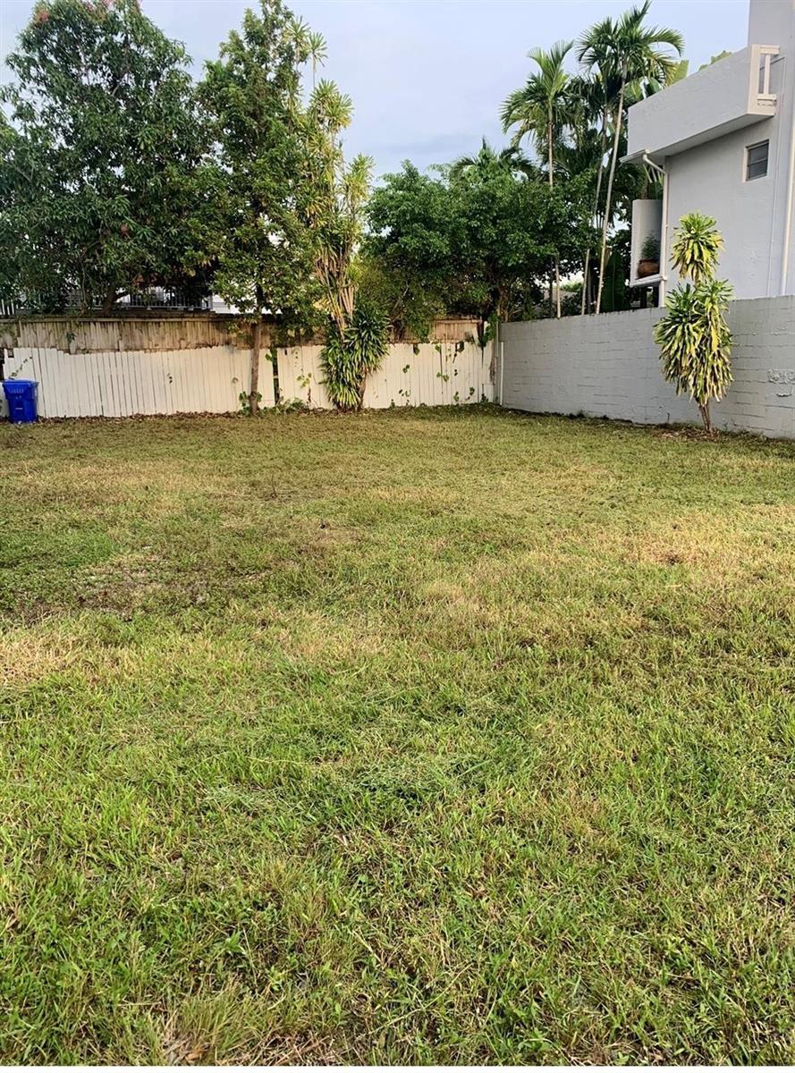 A grassy backyard features a white wooden fence, a concrete wall, and several trees — 2735 SW 32nd Avenue, Miami FL 33133, MIAMI, FL