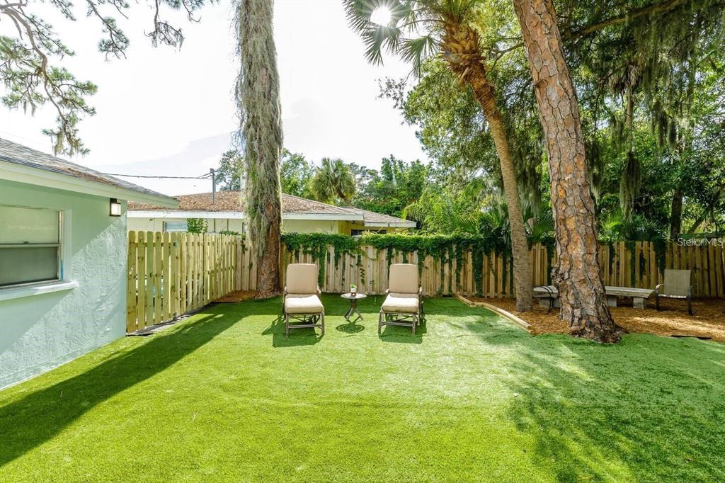 A backyard features artificial turf, two lounge chairs, a wooden fence, and mature trees — 1317 COCOANUT STREET UNIT B, SARASOTA, FL