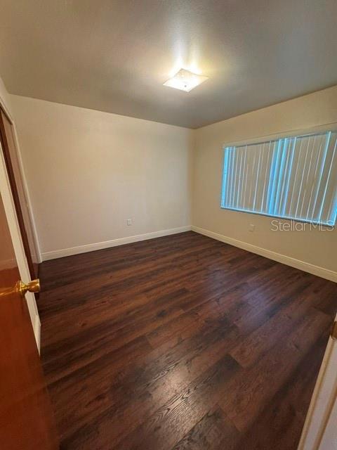 An empty bedroom features dark wood-look flooring, light-colored walls, and a window with vertical blinds — 37623 CAMPHOR DRIVE, DADE CITY, FL