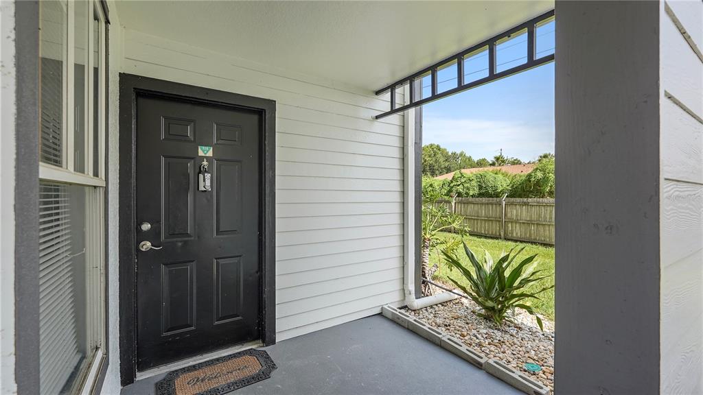 A black front door opens onto a covered porch with a small garden bed — 2204 KEY WEST COURT UNIT 518, KISSIMMEE, FL