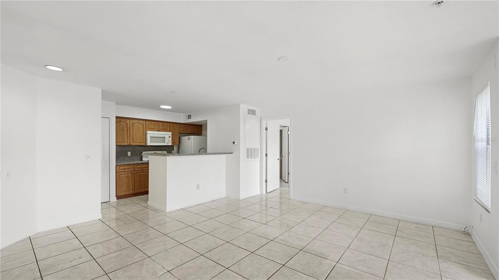An open-concept living area features light-colored tile flooring, white walls, and a kitchen with wood cabinets — 2204 KEY WEST COURT UNIT 518, KISSIMMEE, FL