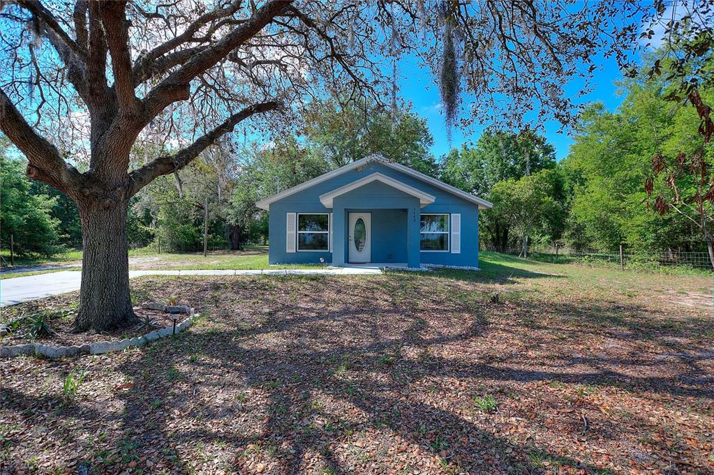 A blue, single-story house with a front porch sits on a grassy lot with trees — 3443 COUNTY ROAD 557A, POLK CITY, FL