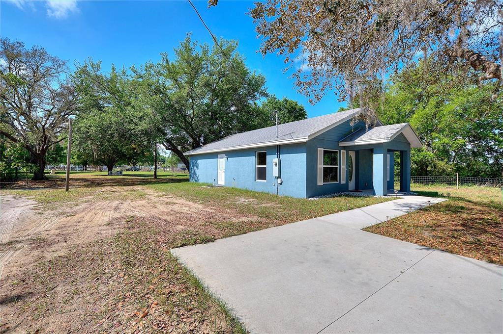 A blue single-story house with a concrete driveway and large trees in the yard — 3443 COUNTY ROAD 557A, POLK CITY, FL