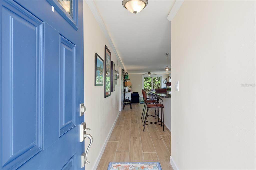 A view from an open blue front door into a hallway with light wood-look flooring — 573 SPANISH DRIVE N, LONGBOAT KEY, FL