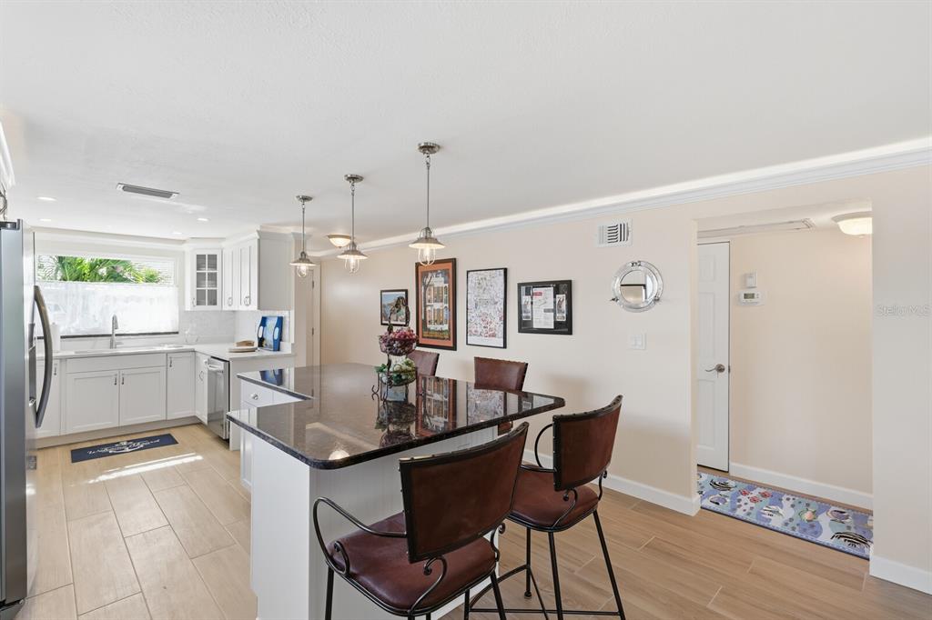 A kitchen features white cabinets, a dark granite island with bar stools, and light flooring — 573 SPANISH DRIVE N, LONGBOAT KEY, FL