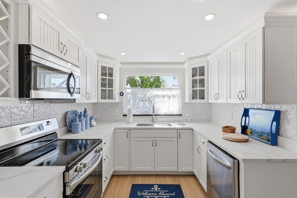 A bright kitchen features white cabinetry, stainless steel appliances, and a window above the sink — 573 SPANISH DRIVE N, LONGBOAT KEY, FL