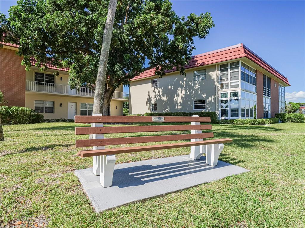A wooden park bench sits on a concrete pad in front of a two-story apartment building — 28 Pine Arbor Lane # 101, Vero Beach FL 32962, VERO BEACH, FL