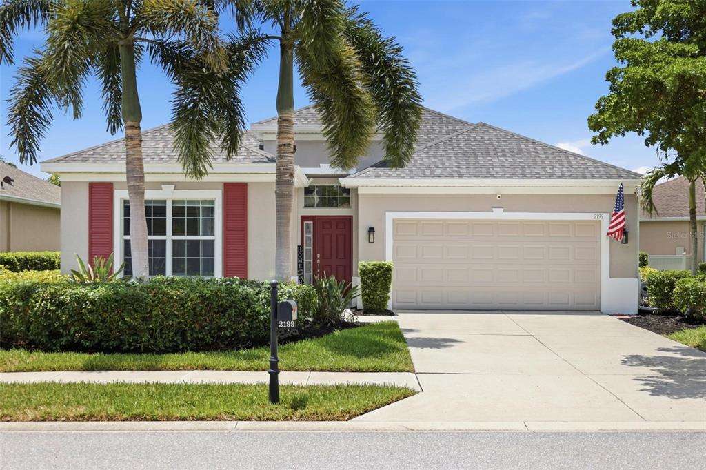 A single-story house with a beige exterior, red shutters, a two-car garage, and palm trees — 2199 TERRACINA DRIVE, VENICE, FL