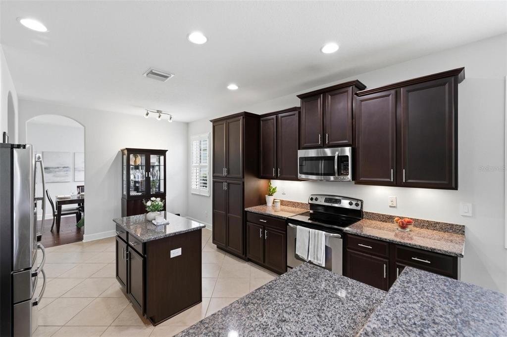 A kitchen features dark wood cabinets, granite countertops, a center island, and stainless steel appliances — 2199 TERRACINA DRIVE, VENICE, FL