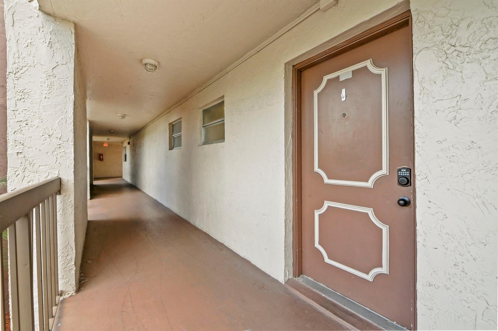 An exterior apartment hallway features a brown door with a keypad lock and textured walls — 7020 Nova Drive # 207d, Davie FL 33317, DAVIE, FL