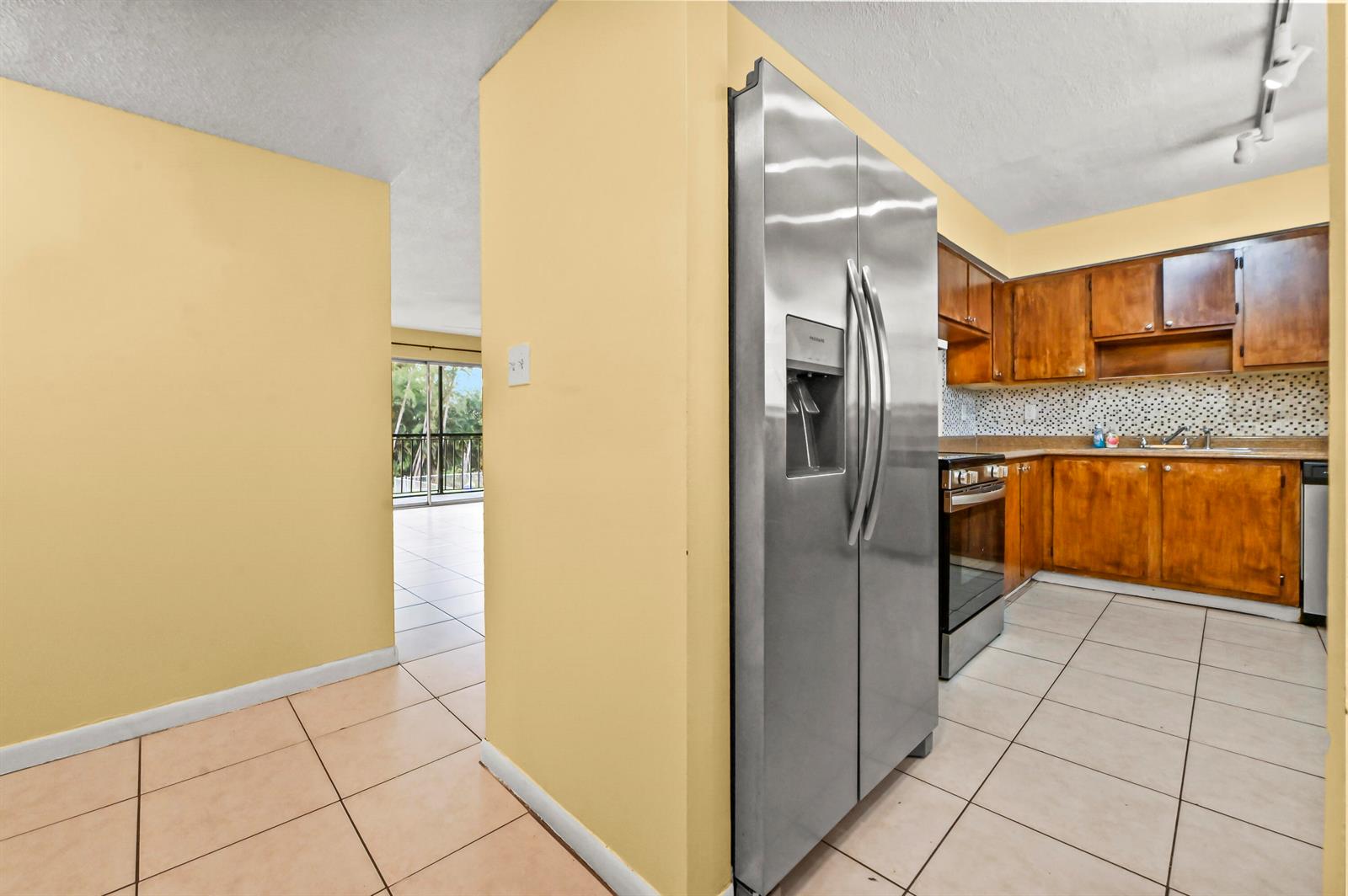A kitchen with wooden cabinets, stainless steel appliances, and tile flooring opens to a balcony — 7020 Nova Drive # 207d, Davie FL 33317, DAVIE, FL
