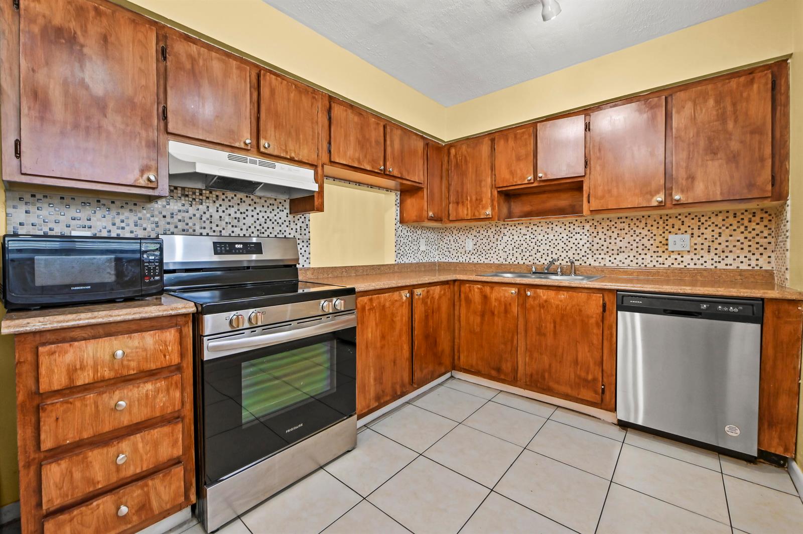 A kitchen features wood cabinets, stainless steel appliances, a tiled backsplash, and light-colored floor tiles — 7020 Nova Drive # 207d, Davie FL 33317, DAVIE, FL