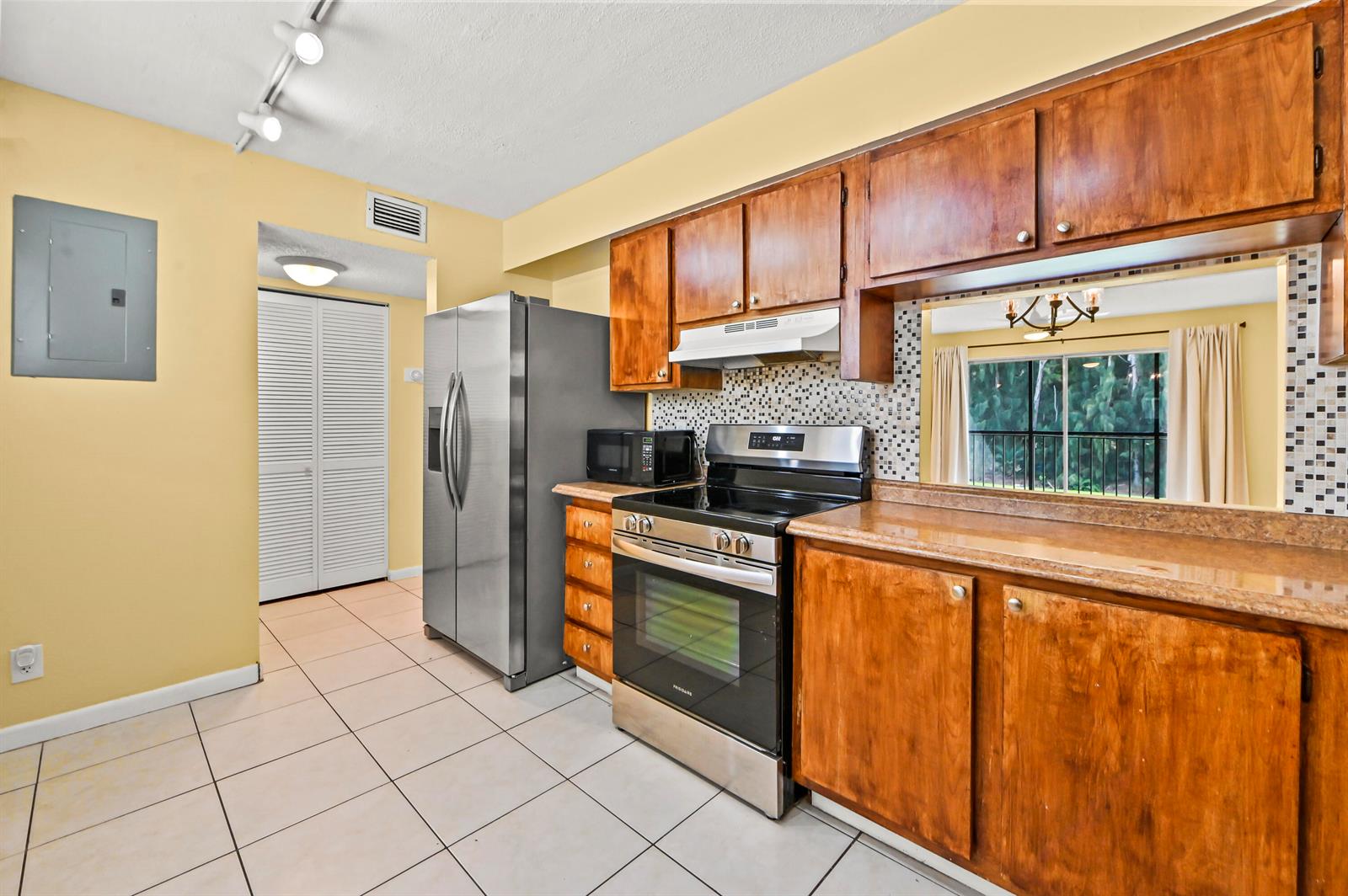 A kitchen features wooden cabinets, stainless steel appliances, tile flooring, and a pass-through window — 7020 Nova Drive # 207d, Davie FL 33317, DAVIE, FL