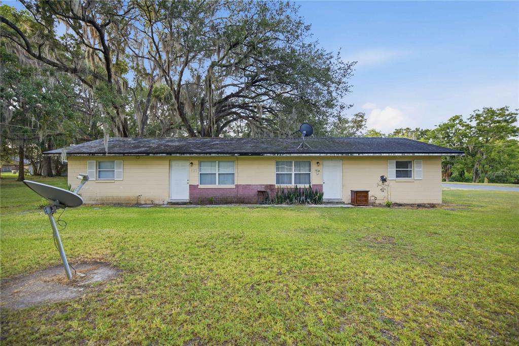 A single-story duplex with a yellow brick exterior, a dark roof, and a large lawn — 421 NE 26TH COURT, OCALA, FL