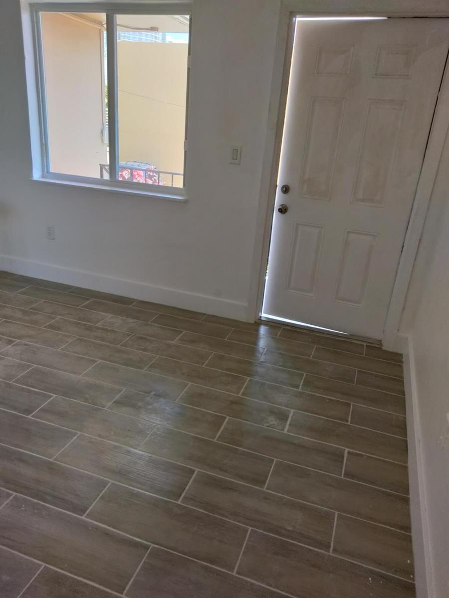 A room with light-colored walls, wood-look tile flooring, a window, and a white entry door — 460 SW 7th Street, Miami FL 33130, MIAMI, FL