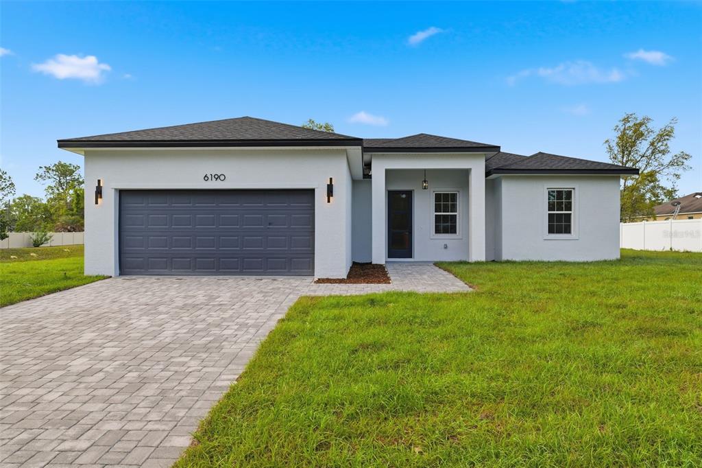 A single-story house with a gray garage, white stucco exterior, and a paved driveway — 6190 SW 144TH PLACE, OCALA, FL