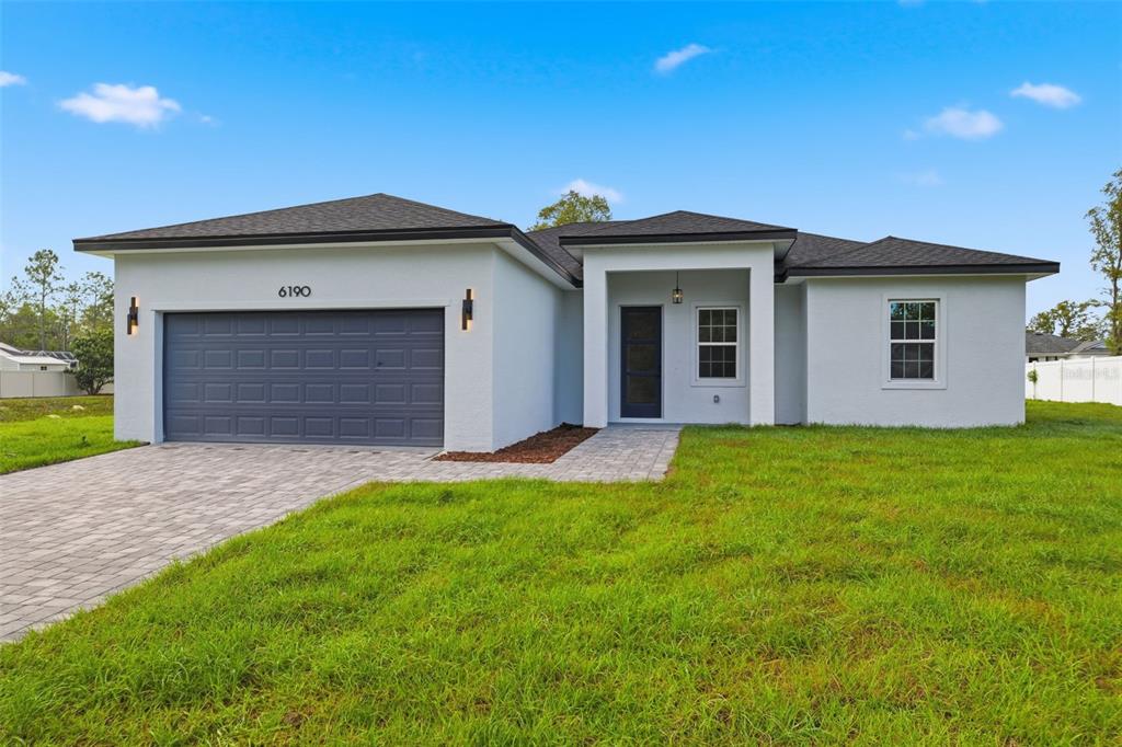 A single-story house with a gray garage, white stucco exterior, and a paved driveway — 6190 SW 144TH PLACE, OCALA, FL