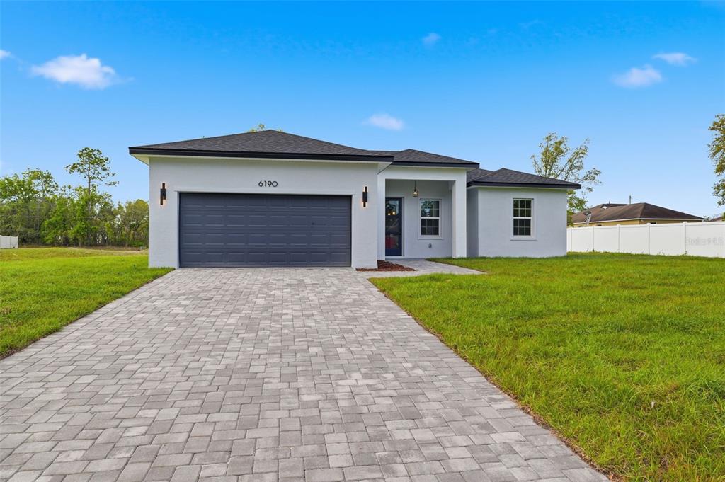 A single-story house with a gray garage, white stucco exterior, and a paved driveway — 6190 SW 144TH PLACE, OCALA, FL
