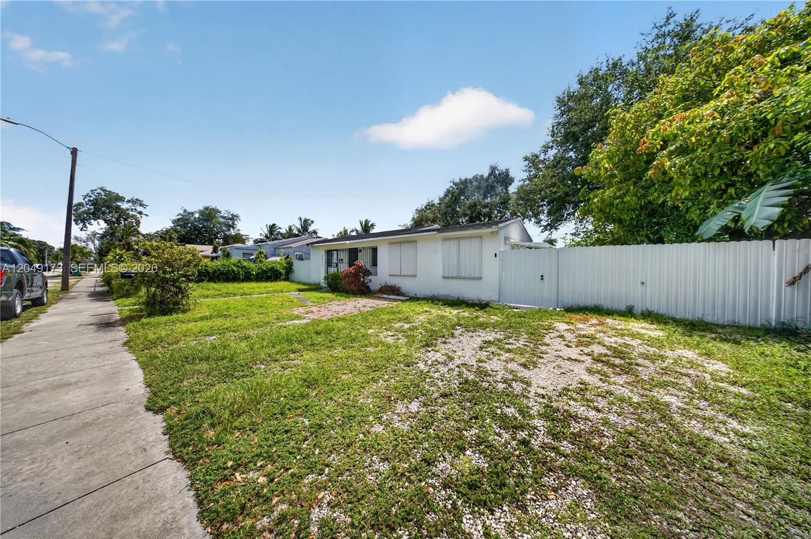 A single-story white house with a gravel driveway and a white metal privacy fence — 9828 NW 26th Ave, Miami FL 33147, MIAMI, FL