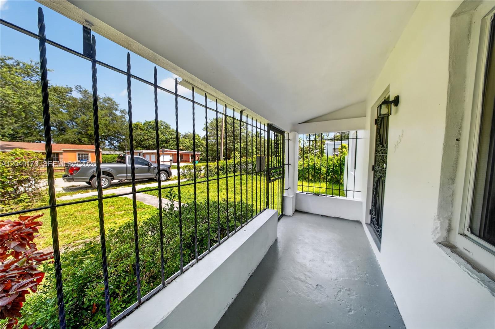 A covered porch features a gray concrete floor, white walls, and black metal security bars — 9828 NW 26th Ave, Miami FL 33147, MIAMI, FL
