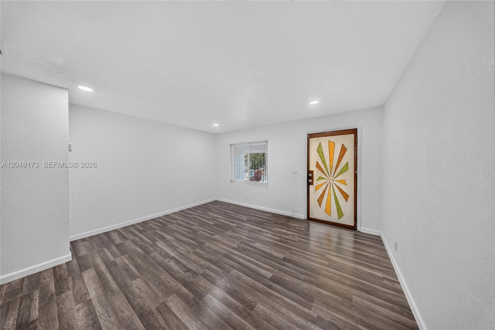 An empty room features wood-look flooring, white walls, recessed lighting, and a decorative front door — 9828 NW 26th Ave, Miami FL 33147, MIAMI, FL