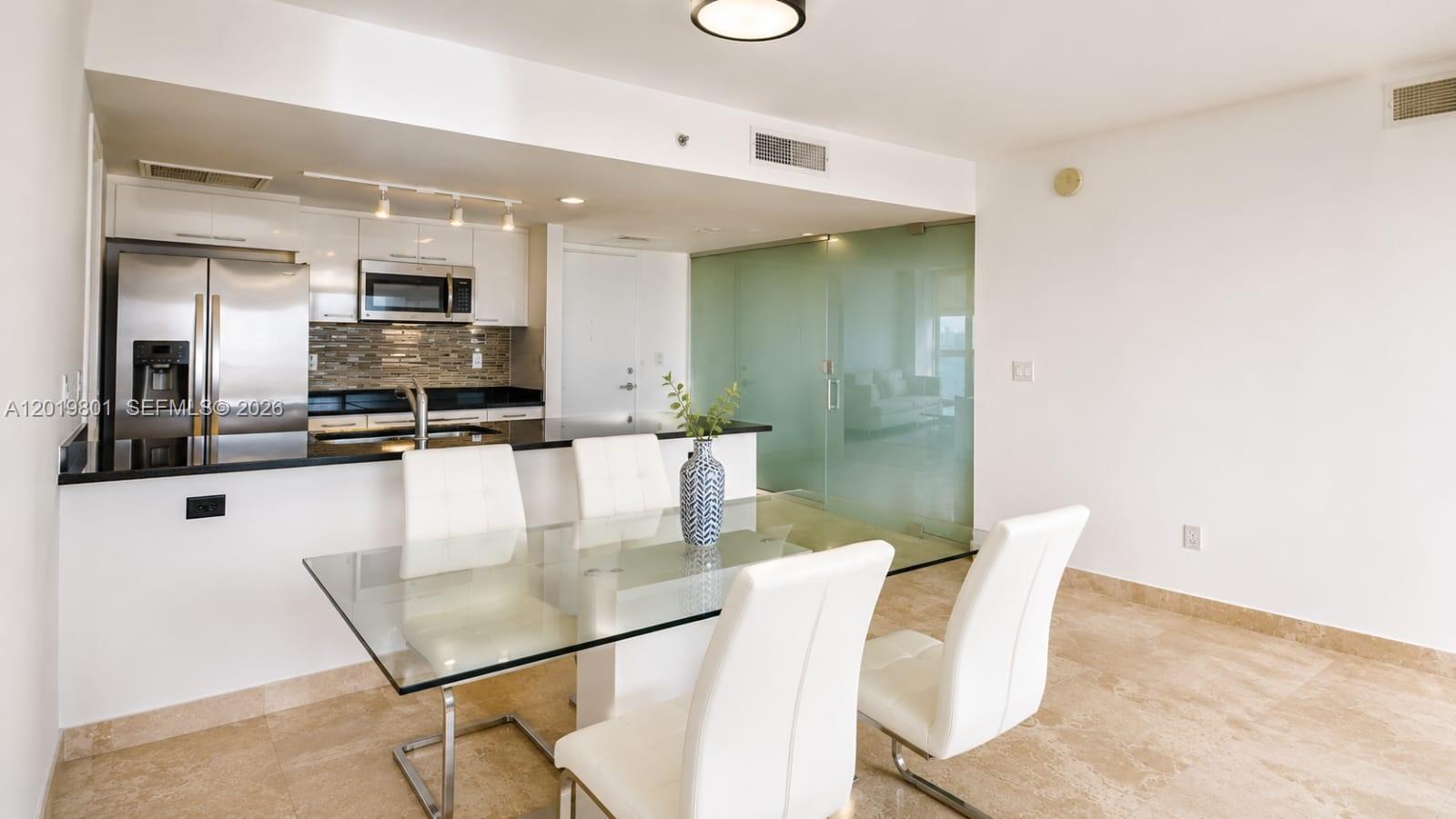 A dining area with a glass table and white chairs sits before an open kitchen — 50 Biscayne Blvd # 4106, Miami FL 33132, MIAMI, FL