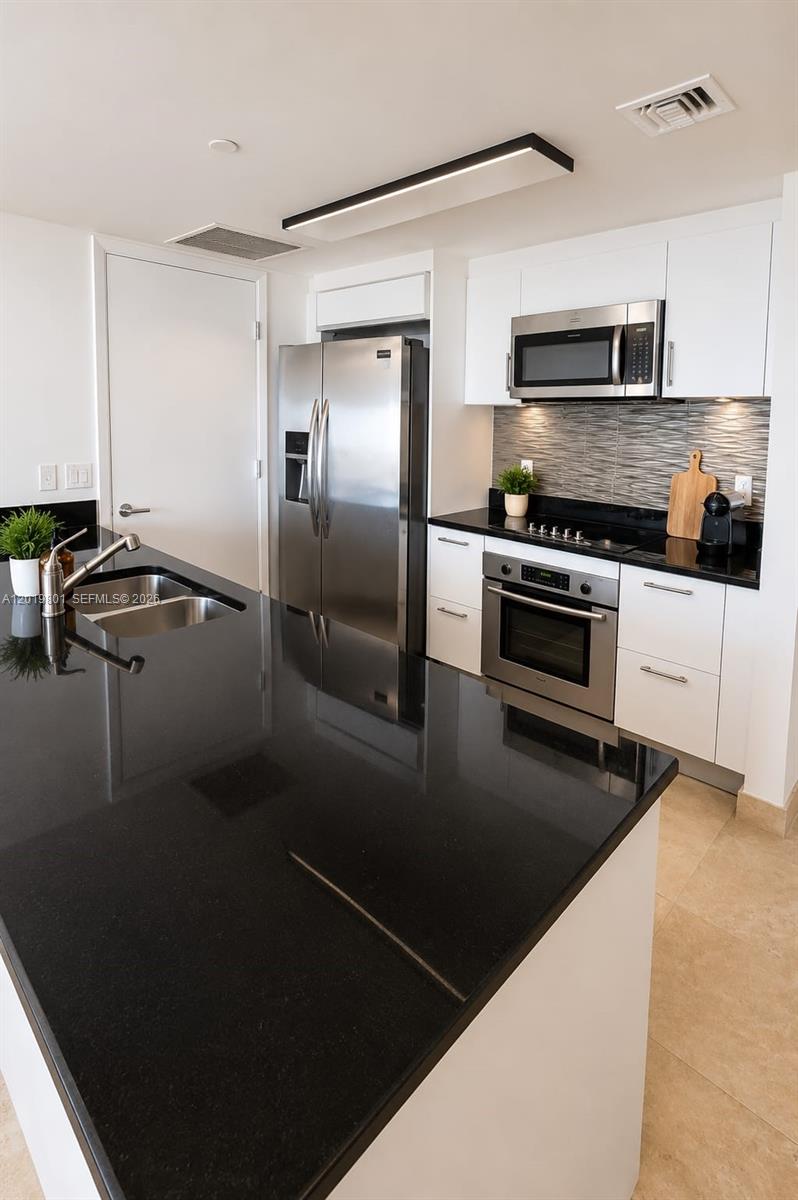 A modern kitchen features white cabinets, black countertops, stainless steel appliances, and a central island — 50 Biscayne Blvd # 4106, Miami FL 33132, MIAMI, FL