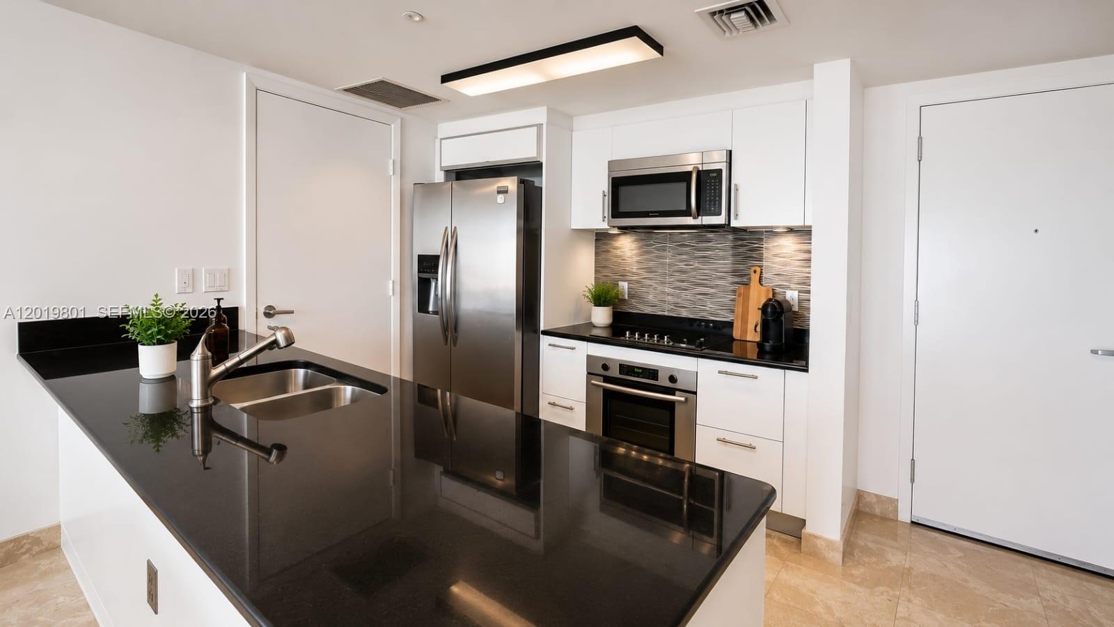A modern kitchen features black countertops, white cabinetry, stainless steel appliances, and a central island — 50 Biscayne Blvd # 4106, Miami FL 33132, MIAMI, FL