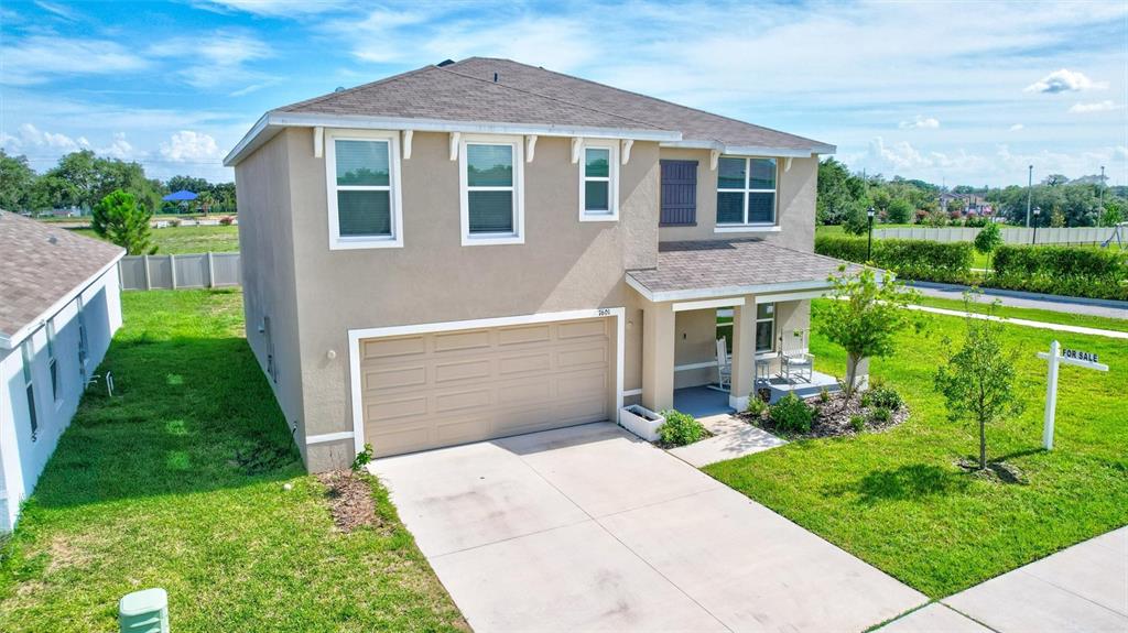 A two-story beige house with a two-car garage and a front porch sits on grass — 7601 ROSEWOOD GARDEN LOOP, TAMPA, FL
