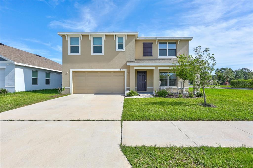 A two-story suburban house with a tan stucco exterior, a two-car garage, and a lawn — 7601 ROSEWOOD GARDEN LOOP, TAMPA, FL