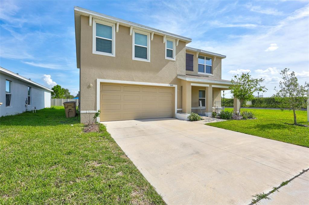 A two-story tan house with a two-car garage and a front porch under a blue sky — 7601 ROSEWOOD GARDEN LOOP, TAMPA, FL