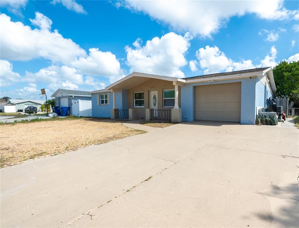 A light blue single-story house features a concrete driveway, a garage, and a covered porch — 1050 DEAL LANE, HOLIDAY, FL