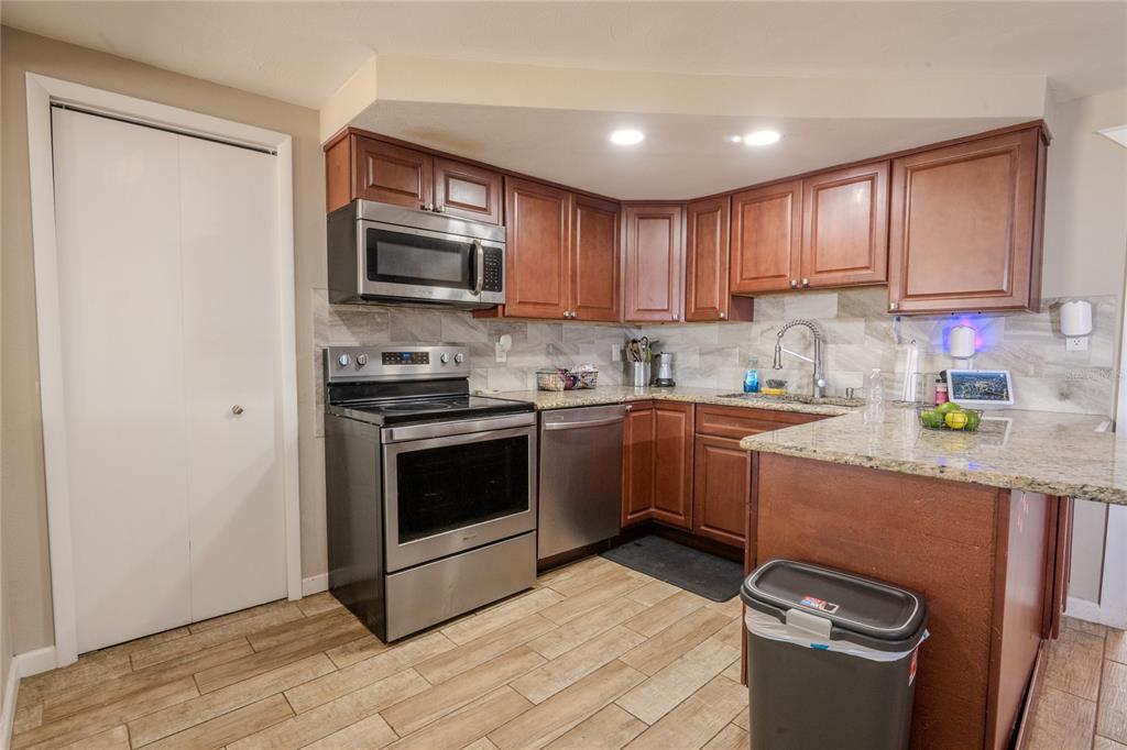 A kitchen features wood cabinets, stainless steel appliances, granite countertops, and light-colored tile flooring — 1050 DEAL LANE, HOLIDAY, FL
