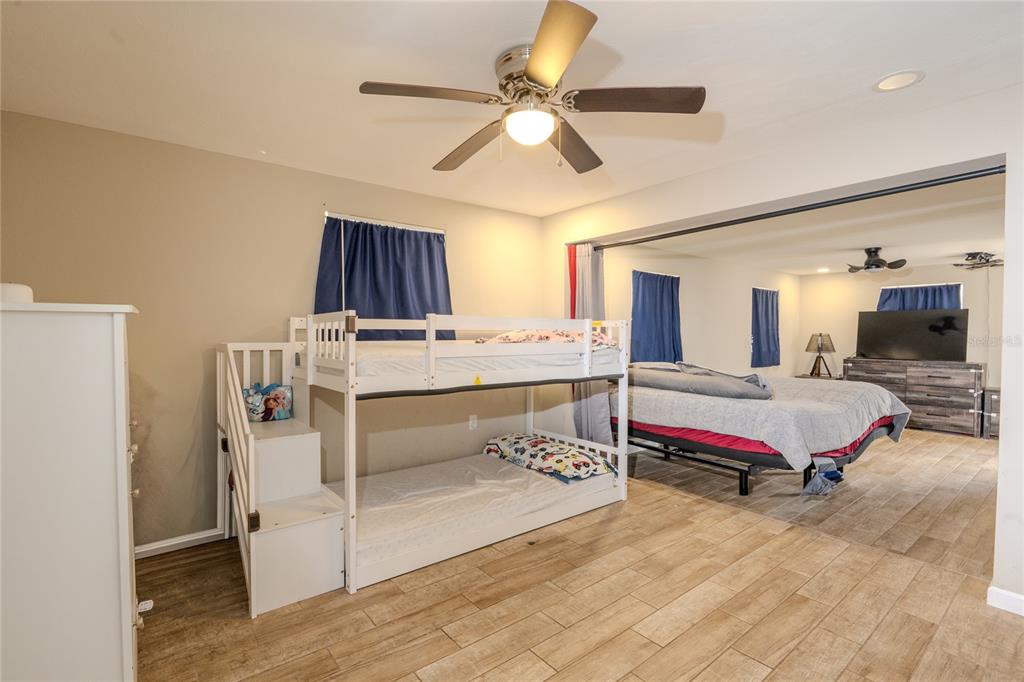 A bedroom features a bunk bed, wood-look tile flooring, and an adjacent sleeping area — 1050 DEAL LANE, HOLIDAY, FL