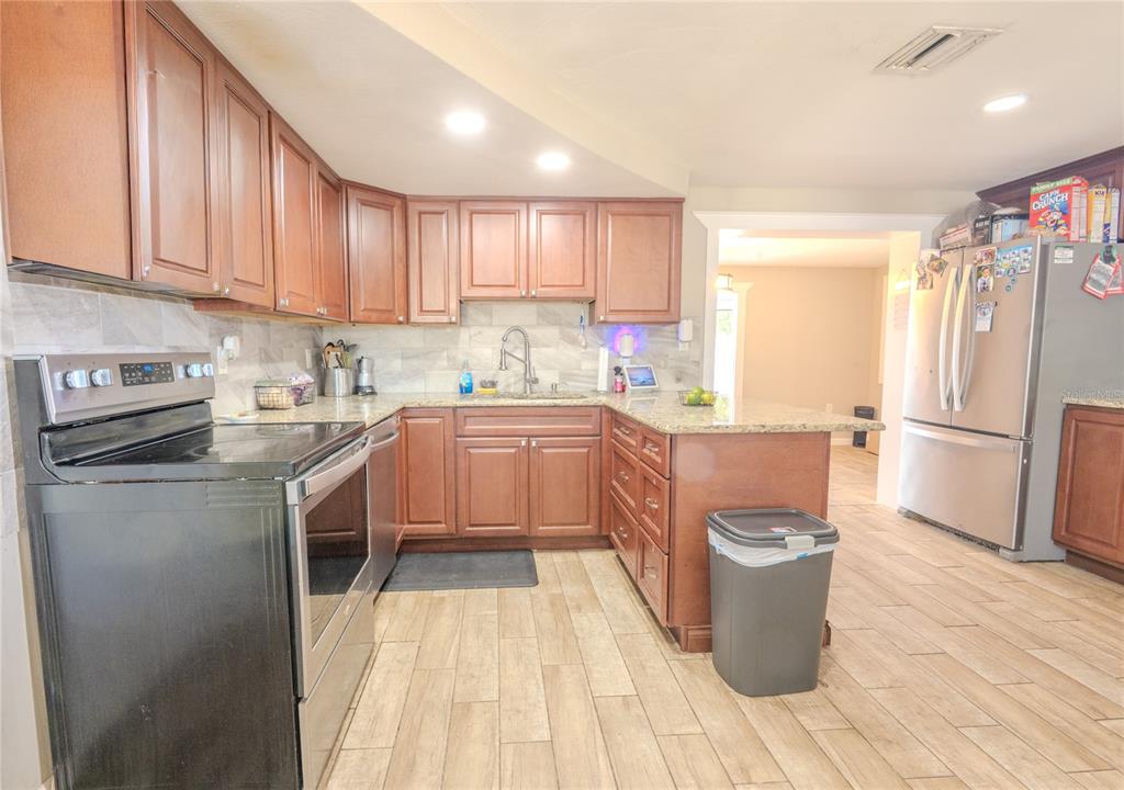 A kitchen features wood cabinets, granite countertops, stainless steel appliances, and light-colored tile flooring — 1050 DEAL LANE, HOLIDAY, FL
