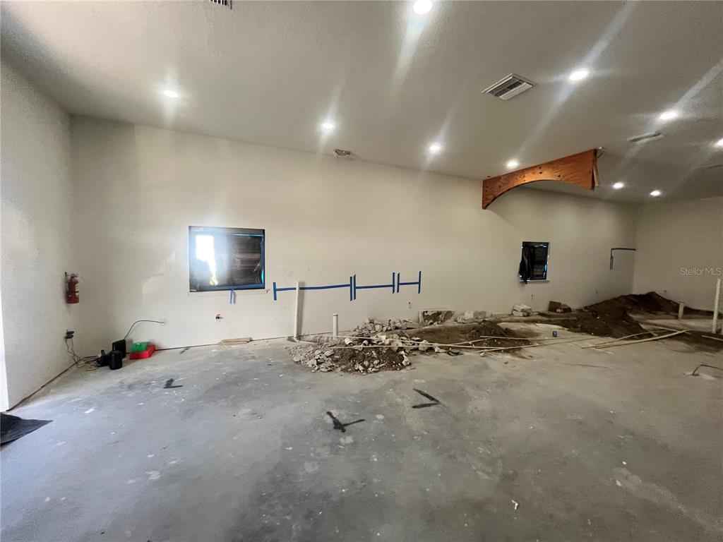 An unfinished room features exposed concrete flooring, plumbing rough-ins, and blue markings on the wall — 1989 21ST STREET NW, WINTER HAVEN, FL