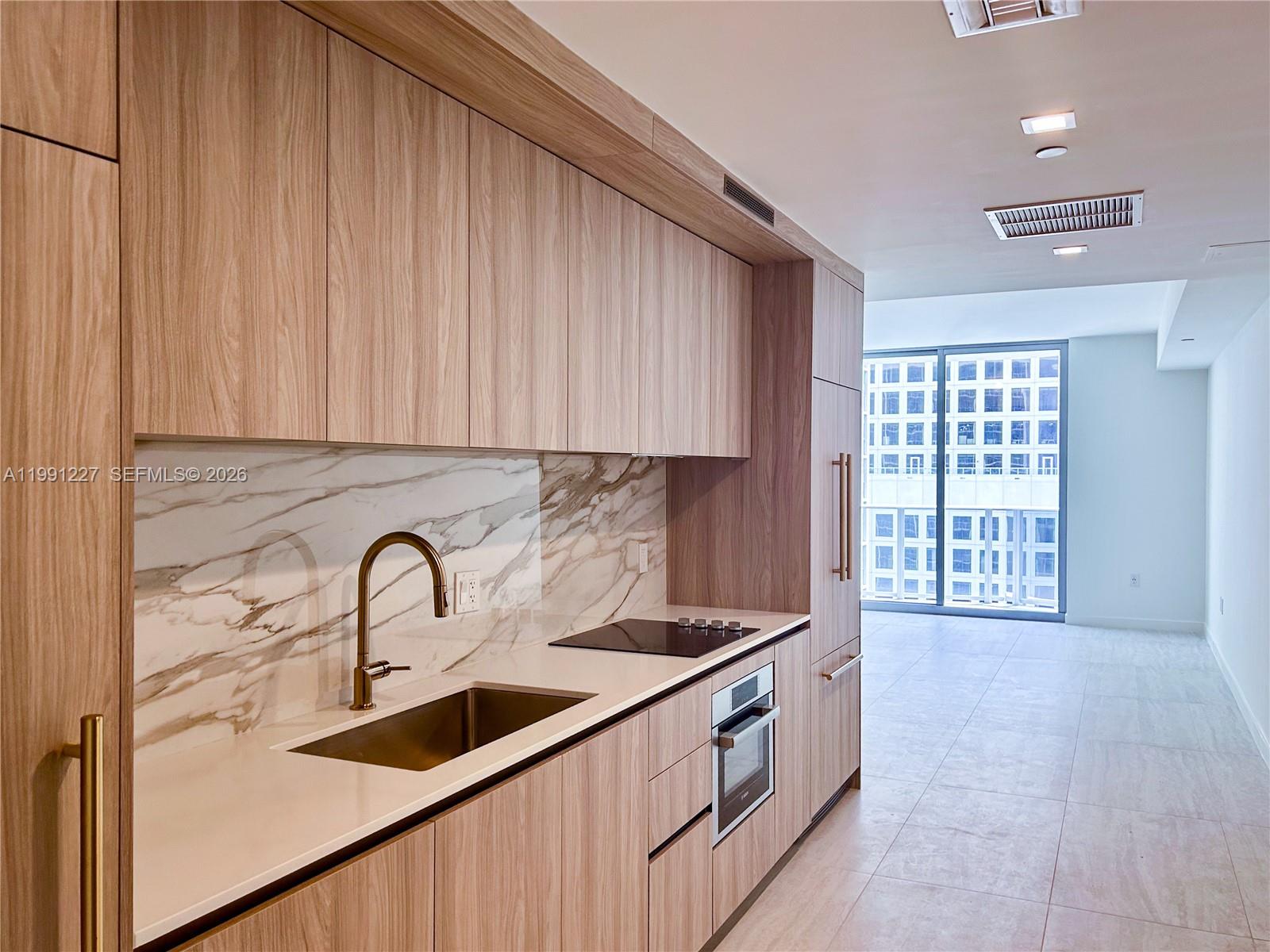 A modern kitchen features light wood cabinetry, a marble backsplash, and a stainless steel sink — 77 SE 5TH ST. # 3614, Miami FL 33131, MIAMI, FL