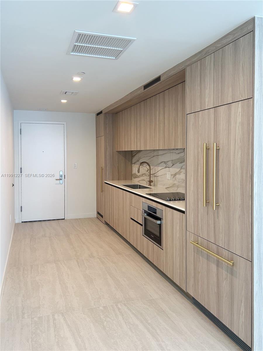 A modern kitchen features wood-grain cabinetry, marble backsplash, and gold hardware — 77 SE 5TH ST. # 3614, Miami FL 33131, MIAMI, FL