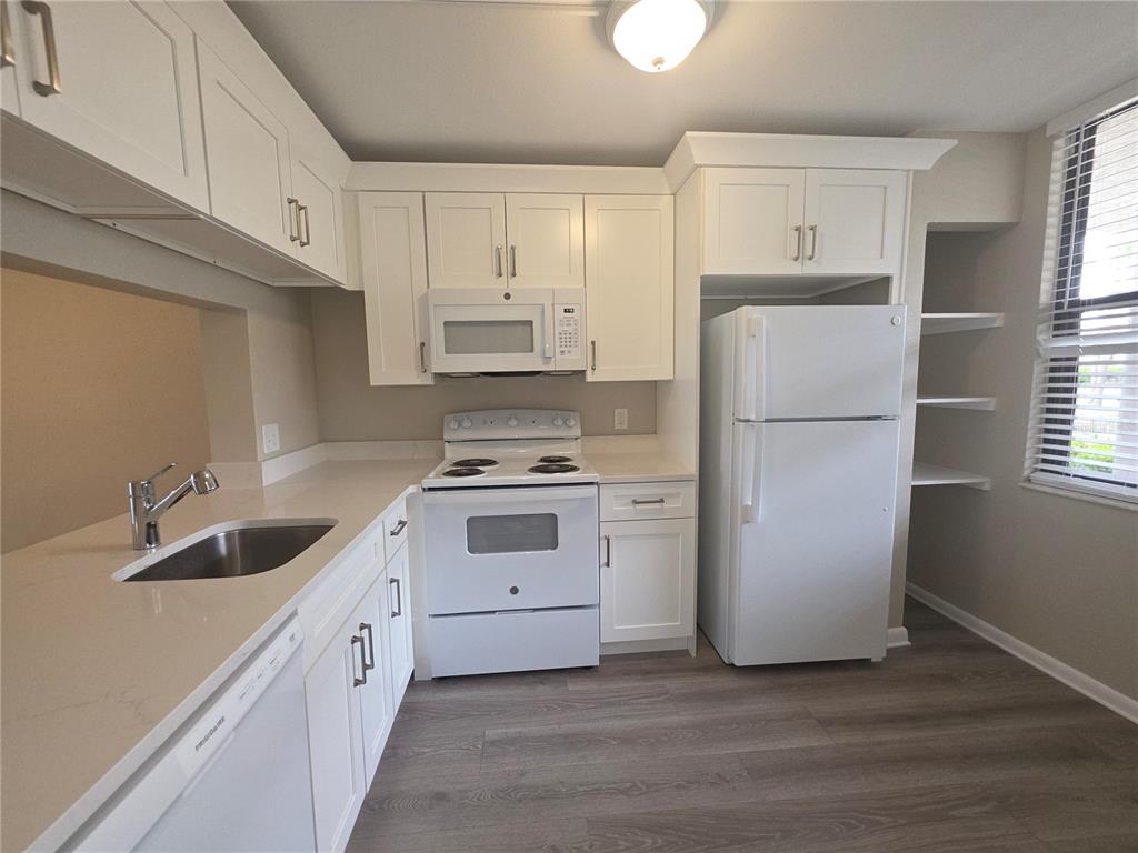 A kitchen features white cabinets, white appliances, light countertops, and wood-look flooring — 2049 SKIMMER COURT W UNIT 311, CLEARWATER, FL