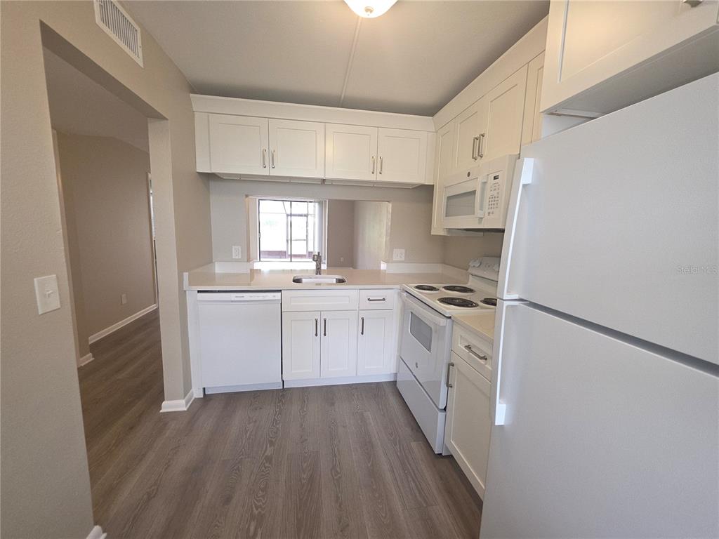 A kitchen with white cabinets, white appliances, and light-colored countertops over wood-look flooring — 2049 SKIMMER COURT W UNIT 311, CLEARWATER, FL