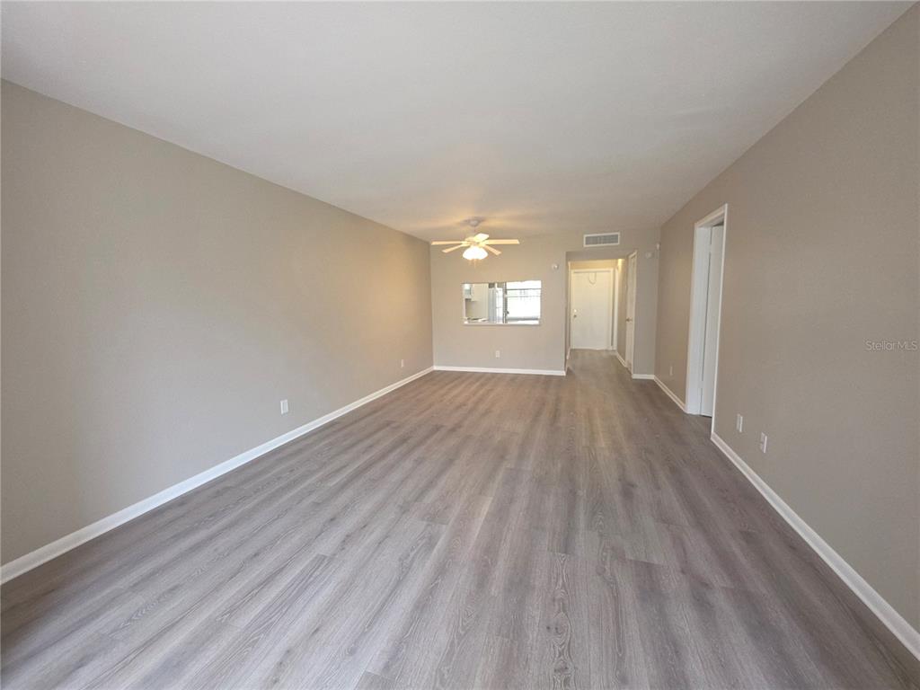 An empty living room features light gray wood-look flooring, beige walls, and a ceiling fan — 2049 SKIMMER COURT W UNIT 311, CLEARWATER, FL