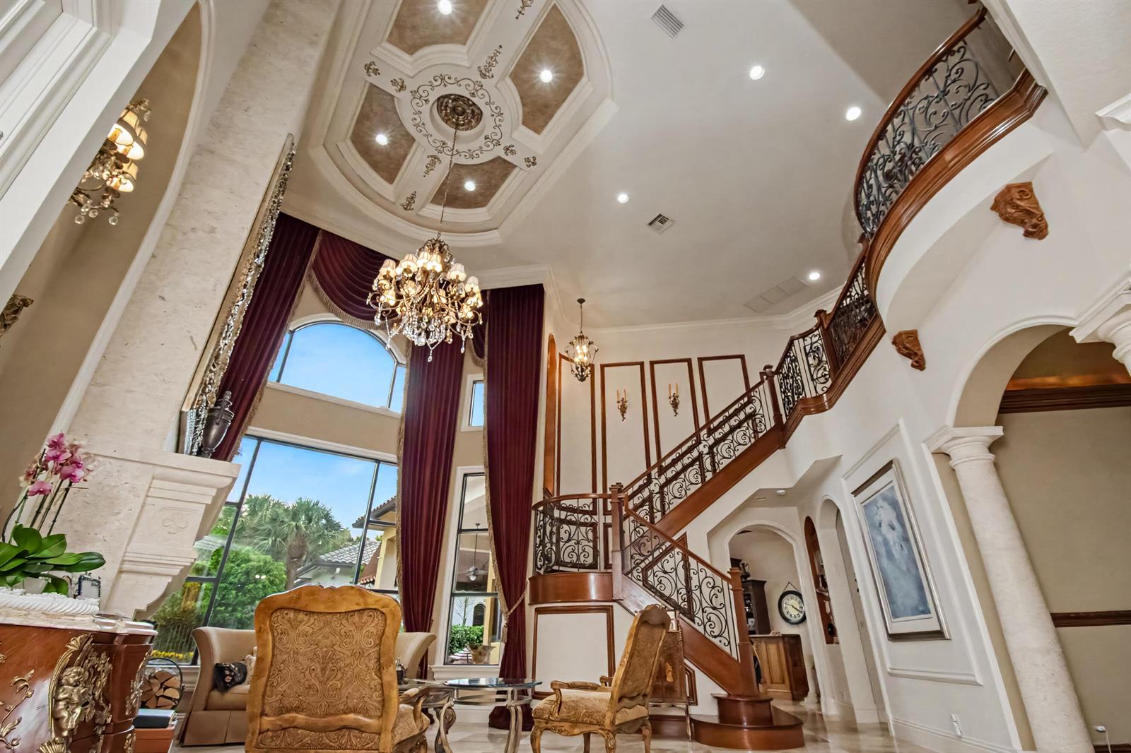 A grand foyer features a curved staircase, ornate ceiling, crystal chandeliers, and floor-to-ceiling windows — 17690 Middlebrook Way, Boca Raton FL 33496, BOCA RATON, FL