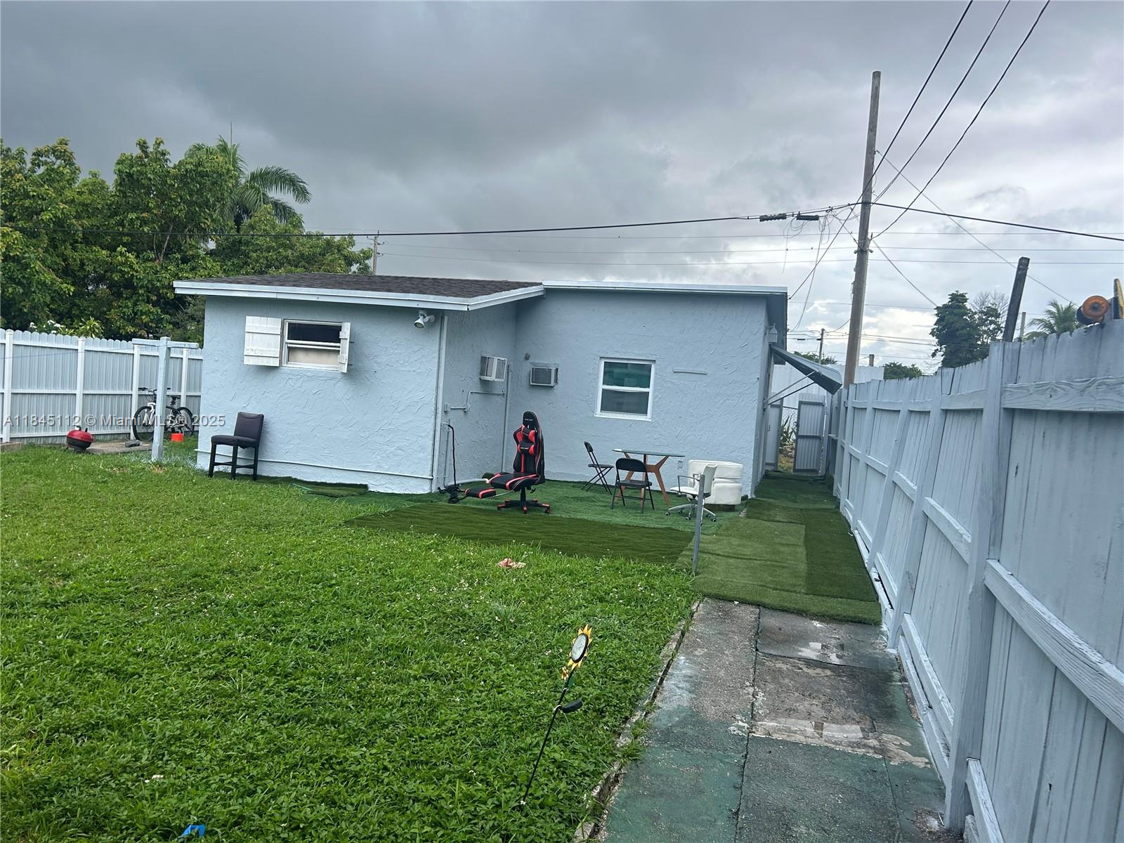 The exterior of a light blue house features a small backyard with artificial turf patches — 2708 NW 22nd Ct, Miami FL 33142, MIAMI, FL