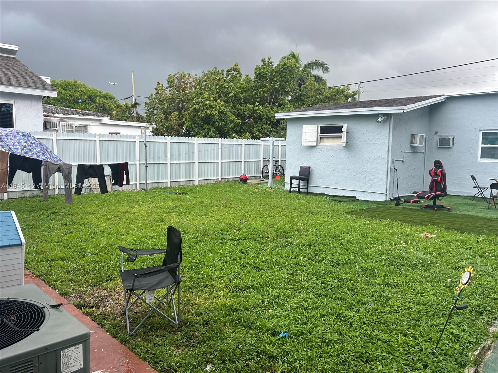 A backyard features a grassy lawn, a white fence, a small shed, and outdoor furniture — 2708 NW 22nd Ct, Miami FL 33142, MIAMI, FL