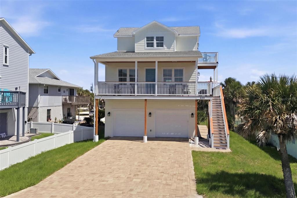 A three-story coastal house features a paved driveway, two garage doors, and an exterior staircase — 856 LADYFISH AVENUE, NEW SMYRNA BEACH, FL