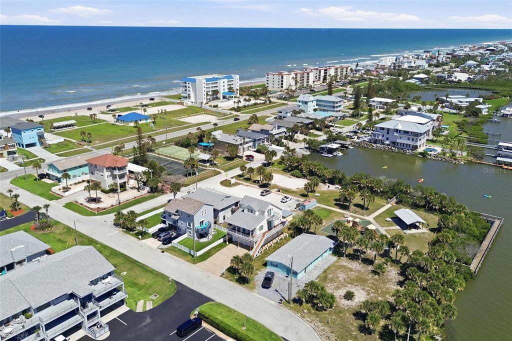 An aerial view shows a coastal neighborhood with houses, a tennis court, and a nearby beach — 856 LADYFISH AVENUE, NEW SMYRNA BEACH, FL