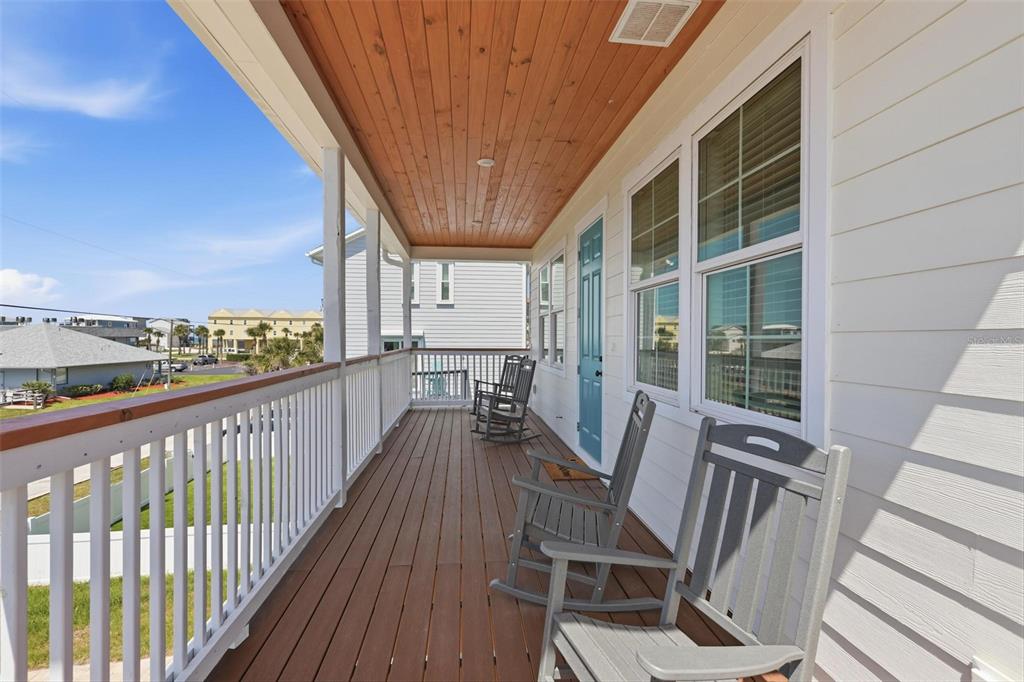 A covered wooden porch features grey rocking chairs and a blue door on a sunny day — 856 LADYFISH AVENUE, NEW SMYRNA BEACH, FL