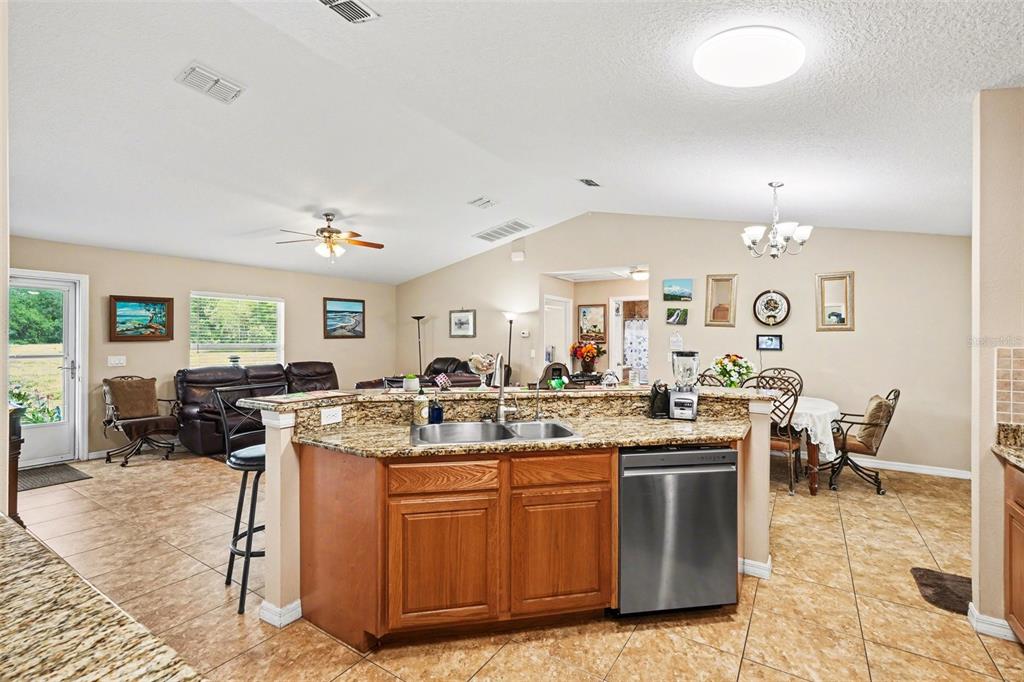 A kitchen with granite countertops and wood cabinets overlooks an open-concept living and dining area — 3147 SYDNEY DOVER ROAD, DOVER, FL